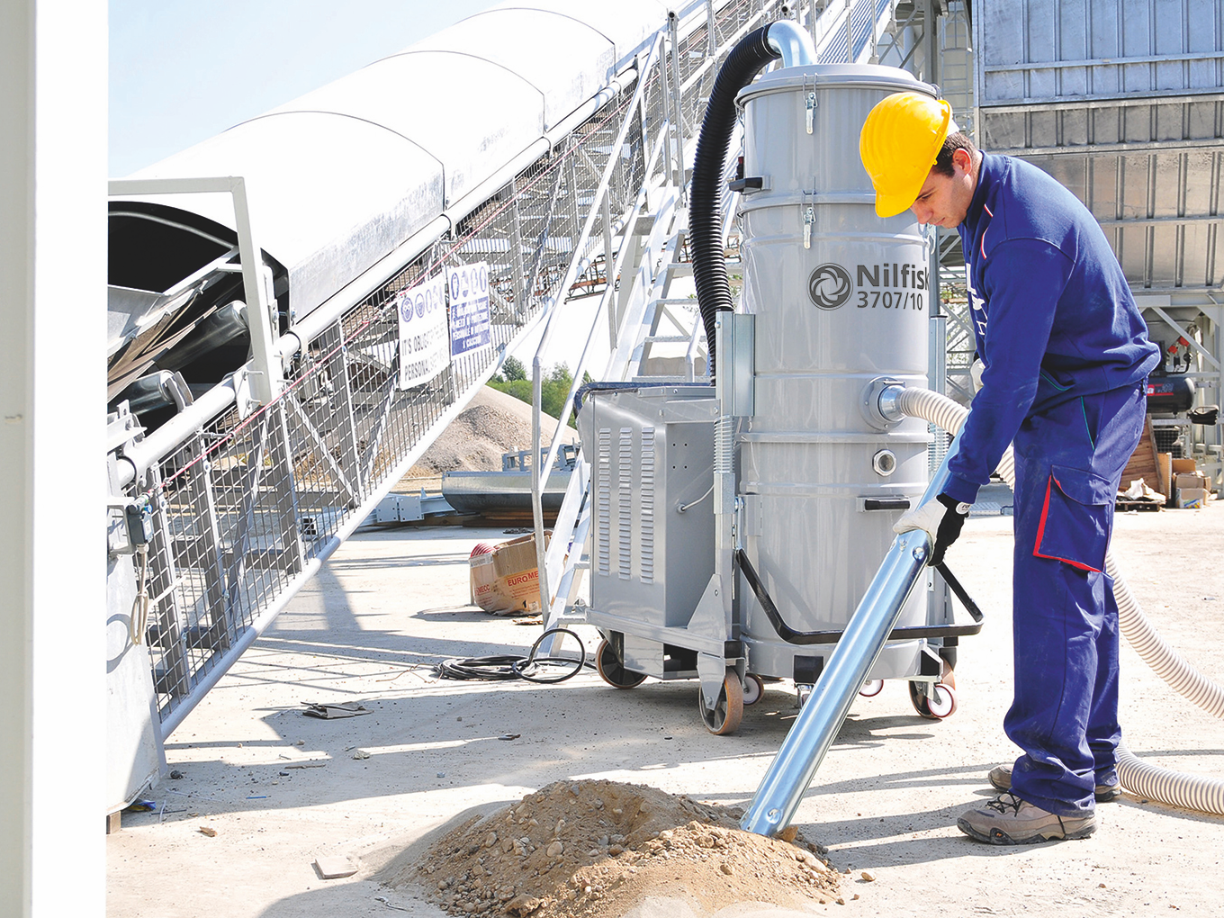 Mining worker managing dust around a conveyor system using industrial cleaning equipment.